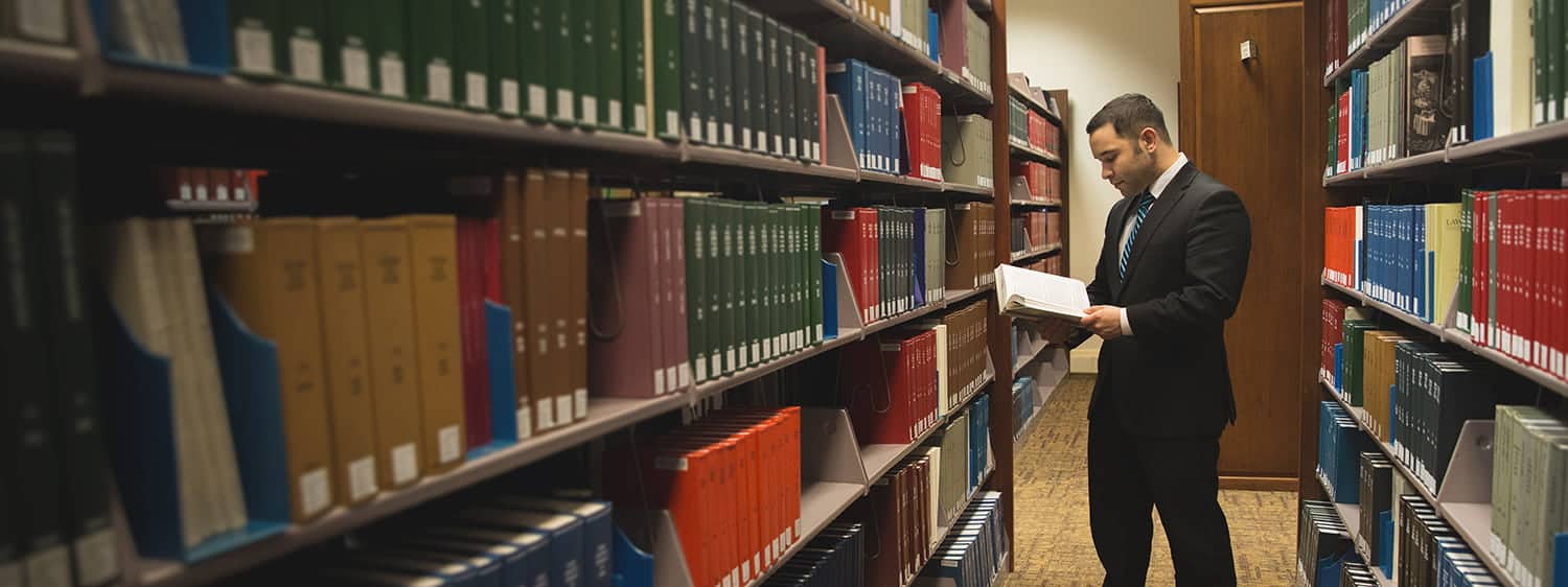 A graduate at the library: Explore the online MA in Law - International Business Transactions program offered by Regent.