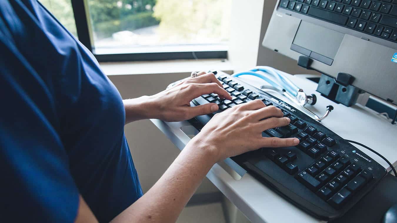 A healthcare professional typing: Explore Regent's online MS in Health Information Systems Administration degree program.