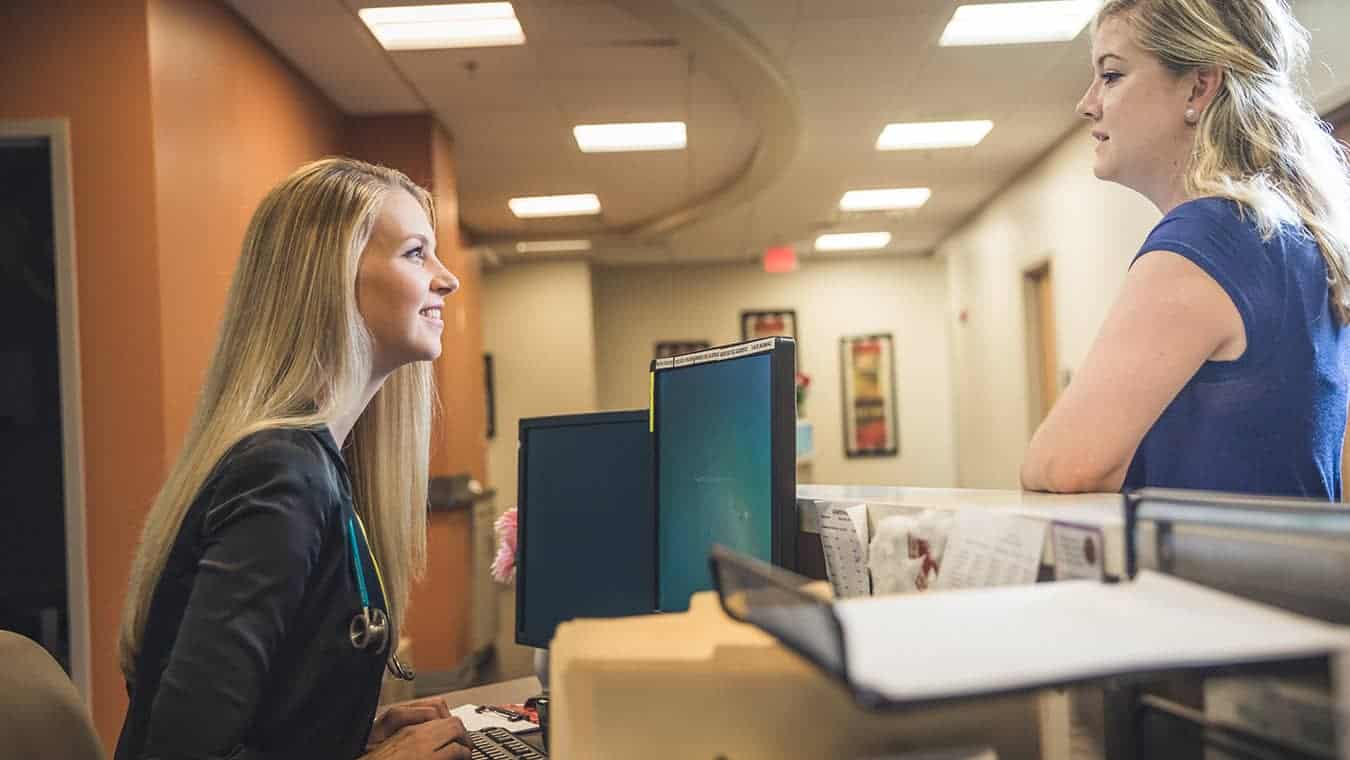 A healthcare professional talks to a guest: Pursue Regent's Nursing Home Administration program online or in Virginia Beach, VA 23464.