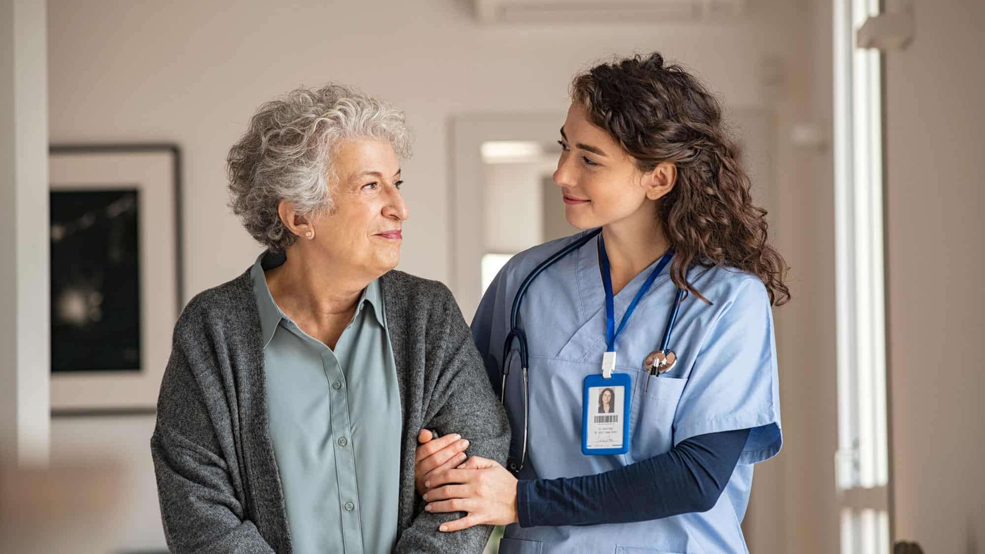 A nurse helps a senior patient. Both smile: Prepare to become a geriatric nurse with a B.S. in Gerontology from Regent University in Virginia Beach, Virginia, 23464.