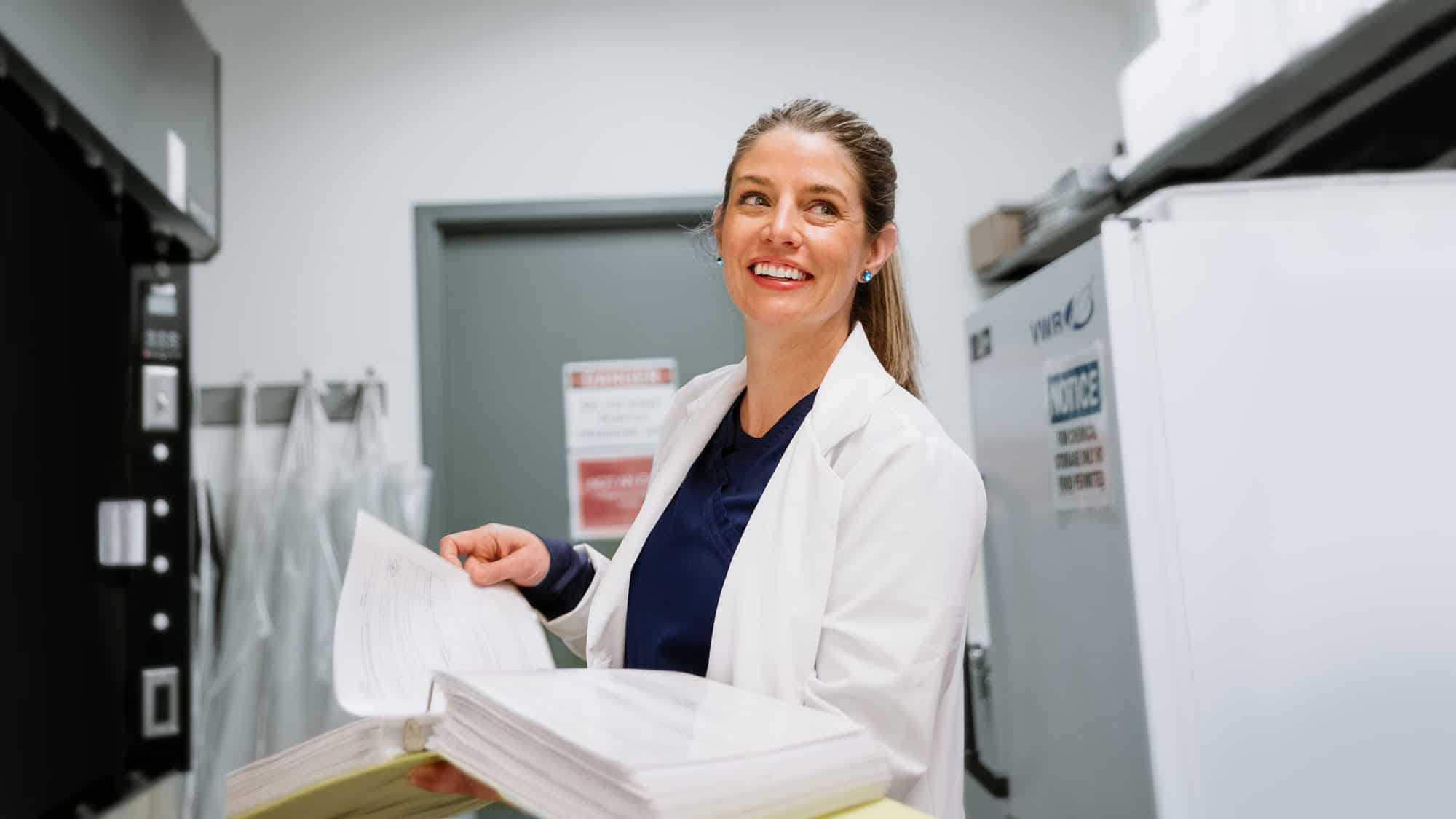 A nurse smiles as she looks through a report. Earn your nursing degree at Regent University in Virginia Beach with a $5,000 scholarship.