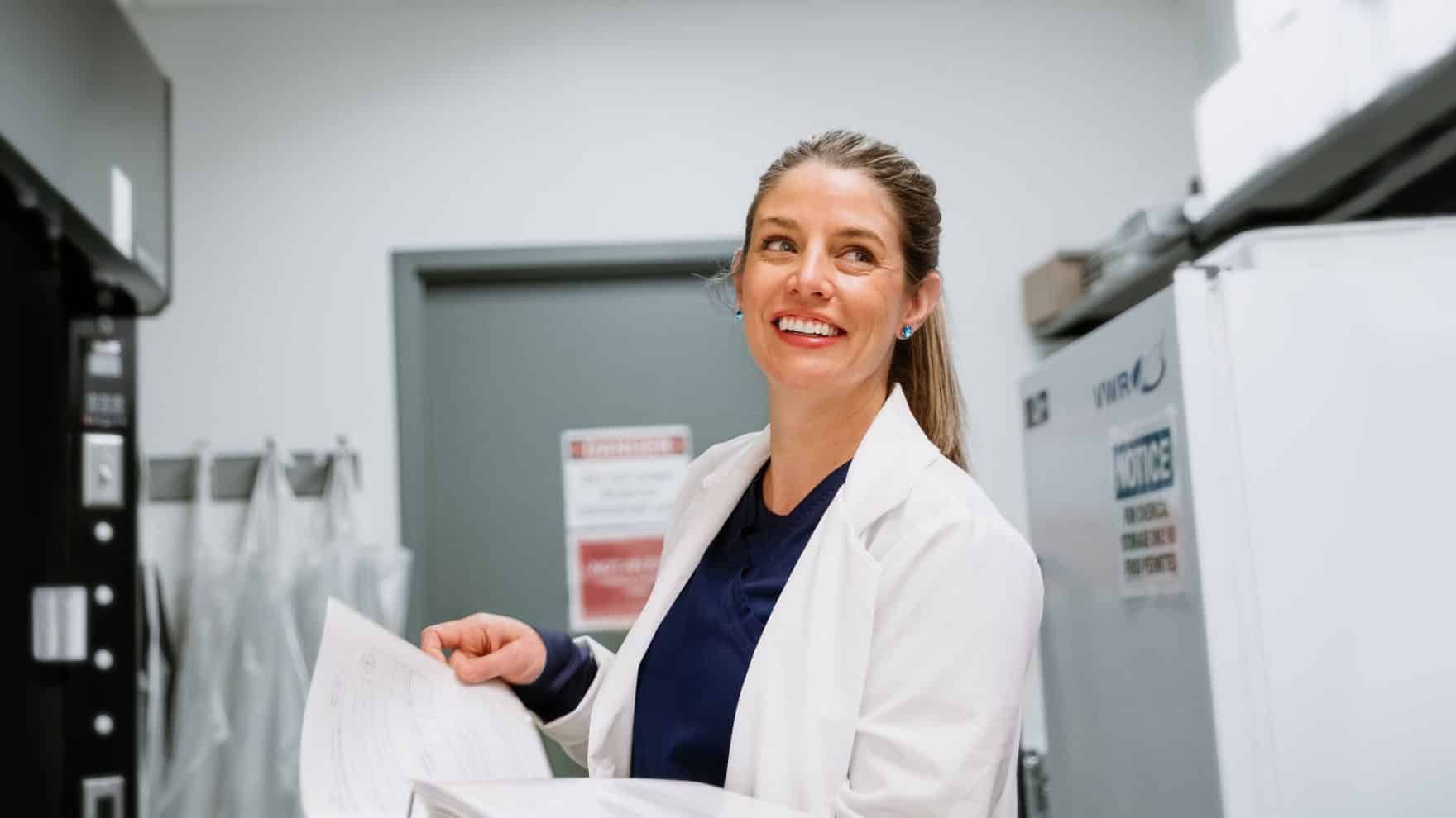 What is an APRN? A female nurse smiles as she looks through papers in a lab.