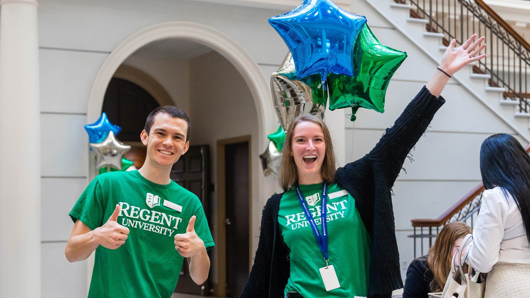 A photo of two Regent University Staff members smiling and waving: Learn more about the readmissions process for returning to Regent.