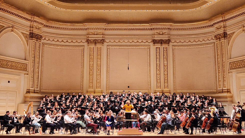 A wide shot in Carnegie Hall that includes the Regent Choir that performed with other choir singers and symphony players that performed together.