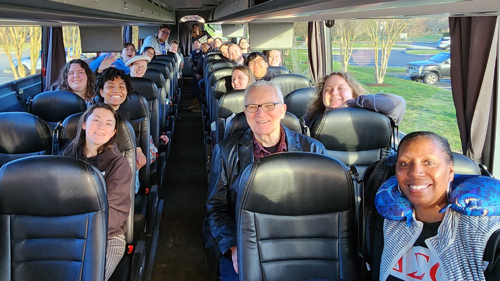 Student and faculty members of the Regent Choir smiling on the charter bus they took from Regent University to Carnegie Hall.