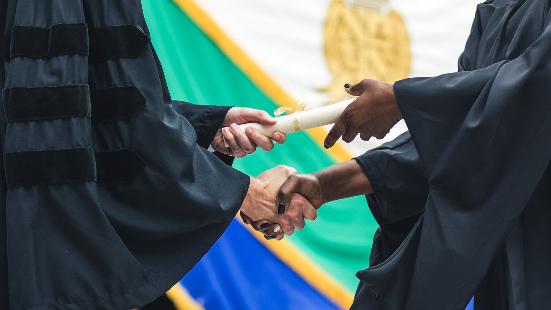 Regent graduate shaking hands while receiving diploma at University commencement ceremony.