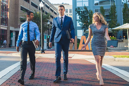 Three Regent University students in professional attire walking across a city crosswalk.