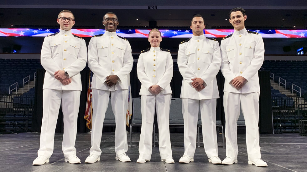 Graduates of Regent University's first NROTC cohort on a stage in uniform: Joshua Ellerson, Solomon Foster-Smith, Kassidy Mayfield, Francisco Morales, and Michael Harrill