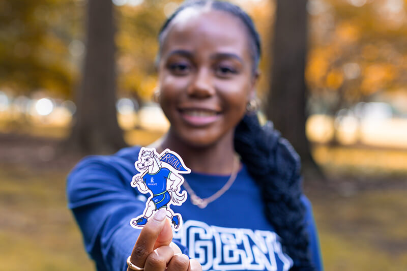 Female student holding Regent Royals mascot sticker.