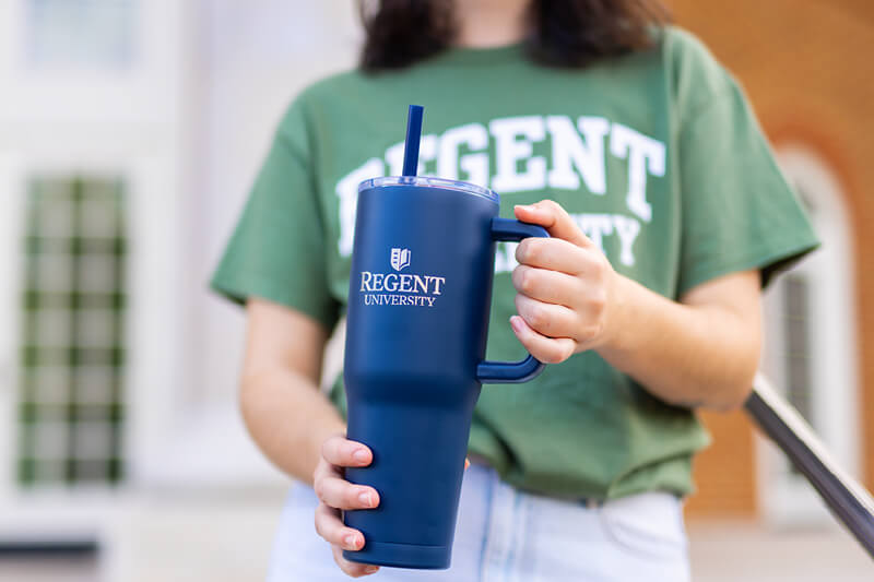 Female student holding Regent Gift Shop tumbler wth straw in Regent blue.