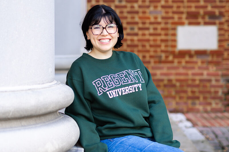 Smiling female student wearing a green hoodie from the Regent Gift Shop.