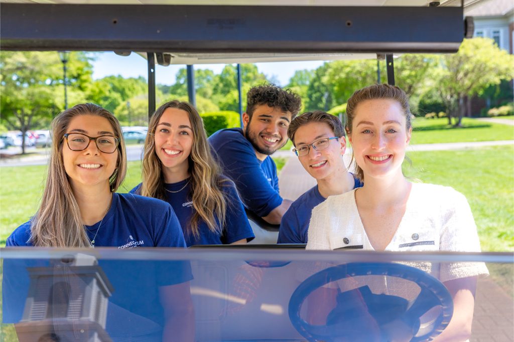 Regent staff smiling and on a golf cart driving around campus.