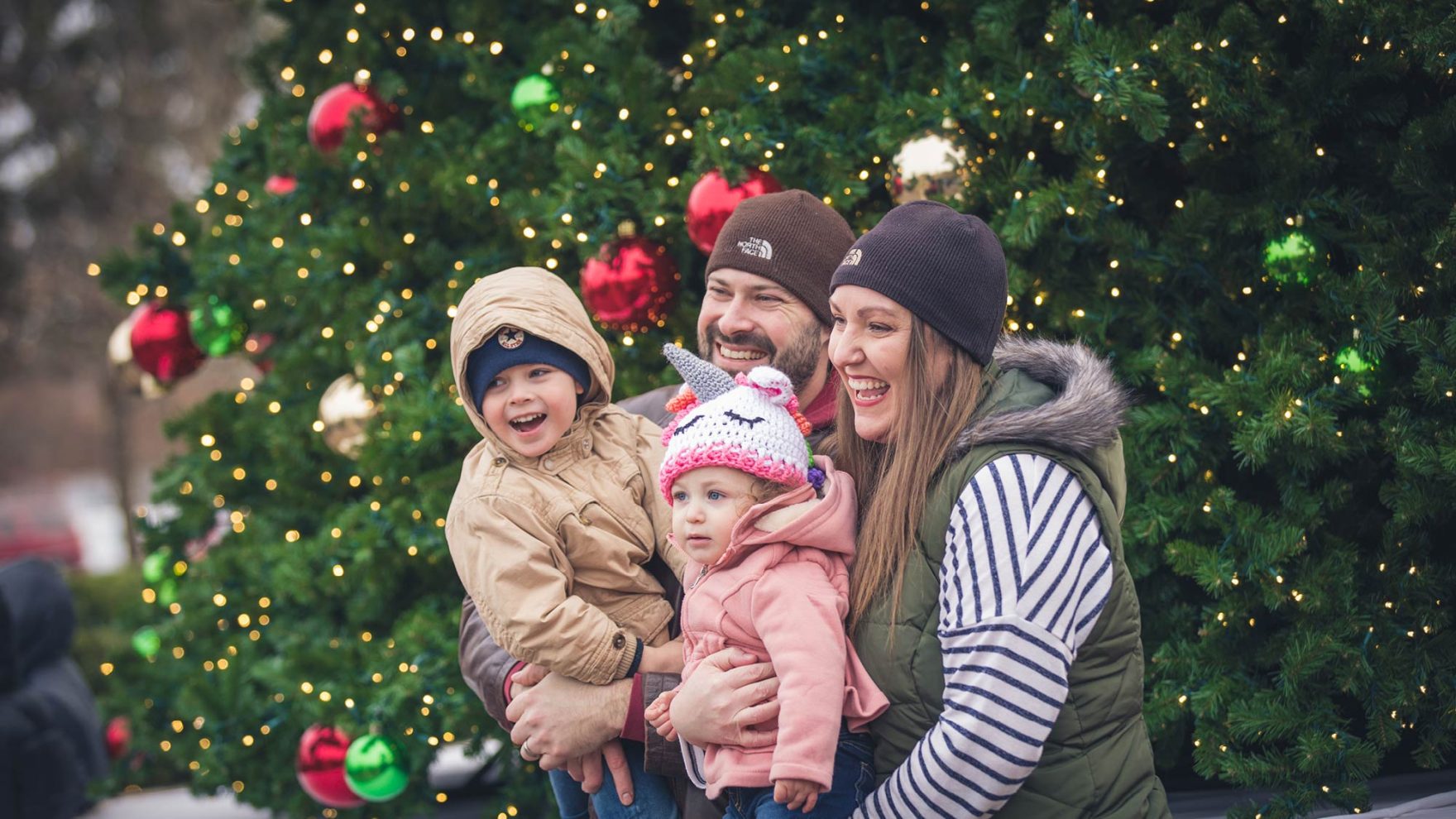 A mother, father, and two children smiling in winter clothes standing in front of a Christmas Tree at an event at Regent University in Virginia Beach, Virginia.