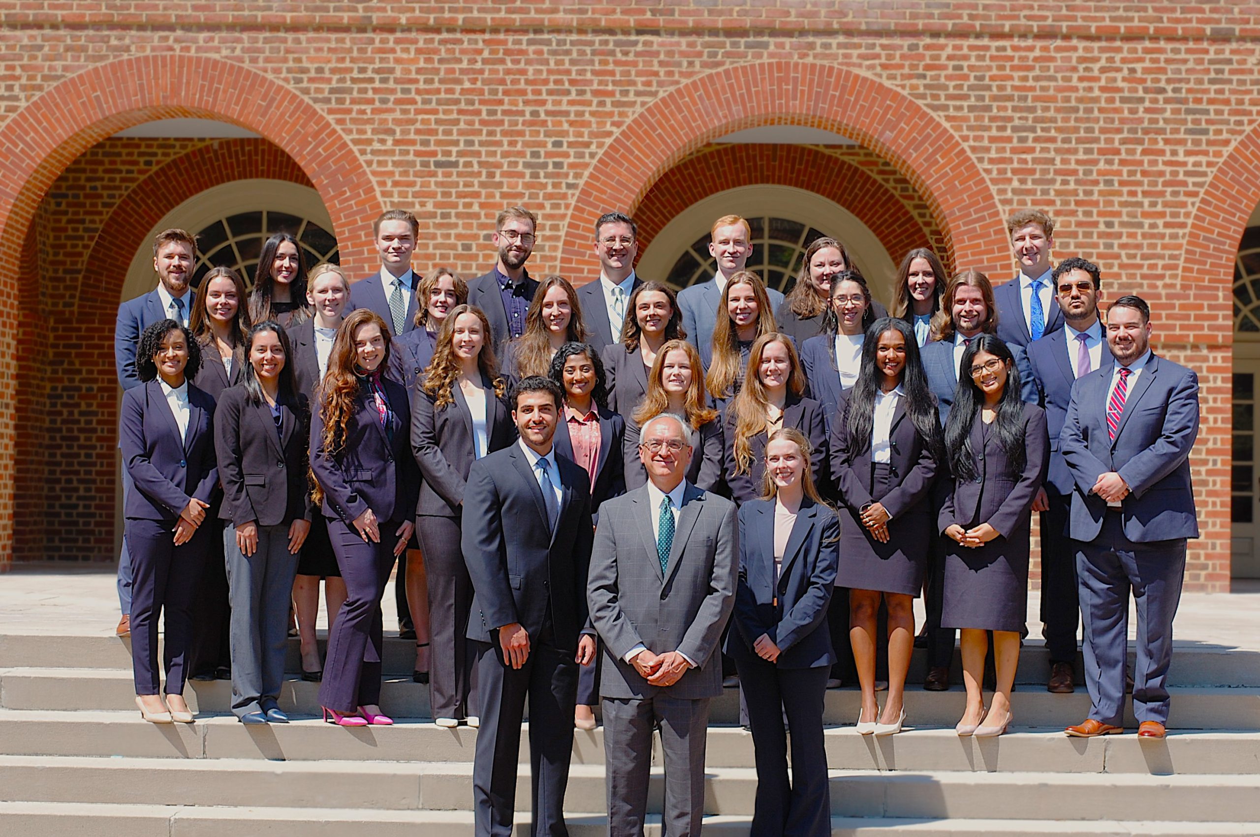 Regent University School of Law students and faculty group photo in professional attire, standing on the steps outside a red-brick academic building.