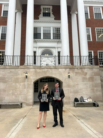 Two students in suits standing in front of a university building with columns