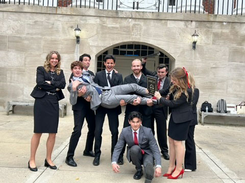 Group of seven students posing indoors by a living plant wall