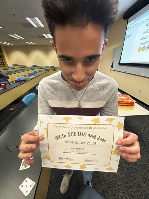 Team photo indoors with students standing in front of a green plant wall