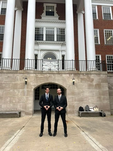 Two students standing with plaques in front of a university building