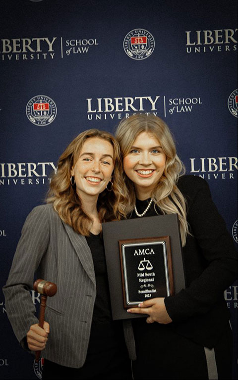 Four students on law school steps with trophies and a gavel
