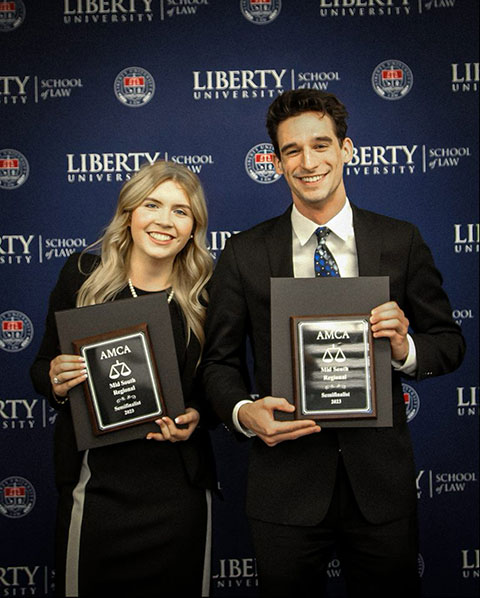 Two team members holding plaques in front of Liberty University School of Law backdrop