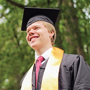 Noah Montgomery smiles in his cap and gown on Regent University’s campus during graduation.