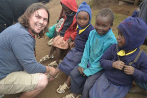 Male volunteer kneeling with group of African children outdoors during mission trip