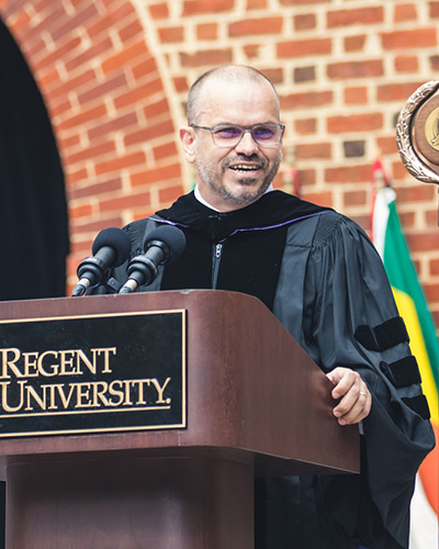 Dr. Corné J. Bekker, dean of Regent University’s School of Divinity, speaking at a podium during commencement.