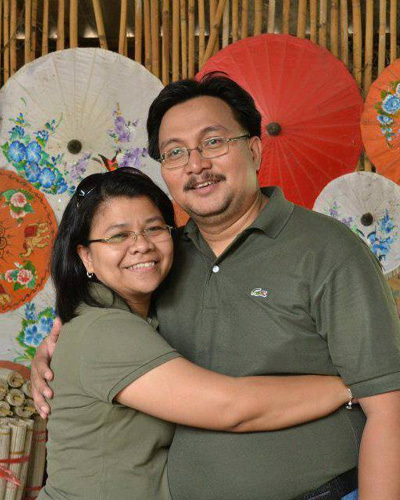 Ethel Servanez-Ligero and her husband Pastor John Ligero smiling together, with colorful traditional Asian paper umbrellas in the background